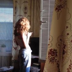 a woman standing in front of a window next to a curtain with flowers on it