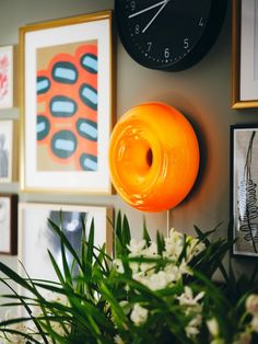 an orange donut is hanging on the wall next to some pictures and flowers with a clock in the background