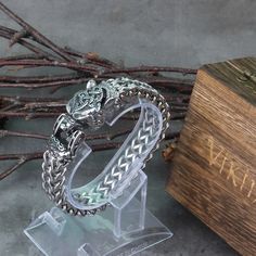 a silver bracelet with a lion head on it sitting next to a wooden box and twig