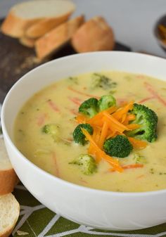 a white bowl filled with broccoli cheese soup next to some bread and crackers