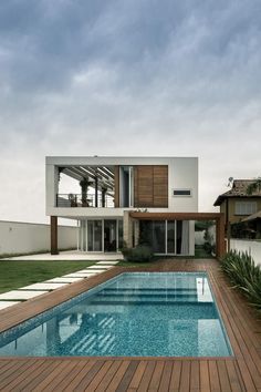 a large swimming pool in front of a house with wooden decking and green grass