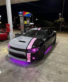 a black and grey car with pink stripes parked at a gas station