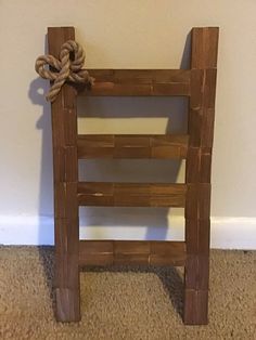 a wooden ladder with rope tied to it on carpeted floor next to white wall