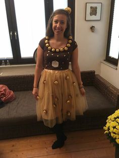 a woman standing in front of a couch wearing a dress with gold buttons on it