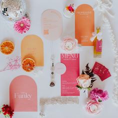 an assortment of wedding stationery and flowers on a white tablecloth with pink and orange accents