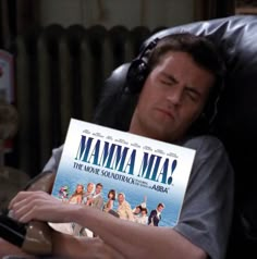 a man sitting in a chair holding up a movie poster with the title mamma mia on it