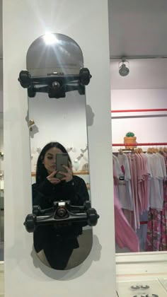 a woman taking a selfie in front of a mirror with clothes on racks behind her