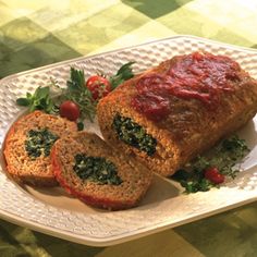 two slices of meatloaf on a white plate with tomatoes and parsley next to it