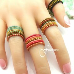 a woman's hand with four different colored rings on her fingers and one is wearing a pink manicure