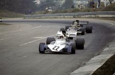 two racing cars driving down a race track with people watching from the sidelines behind them