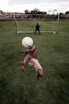 a man jumping up to catch a soccer ball in front of him on the grass