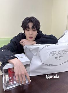 a young man sitting at a table with a bag and some drinks in front of him