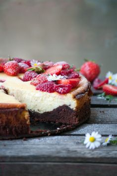 a cheesecake with strawberries on top is sitting on a table next to daisies