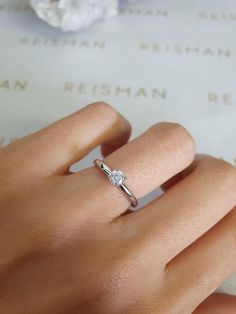 a woman's hand with a diamond ring on top of her finger next to a piece of paper