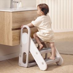 a baby sitting on a step stool next to a sink