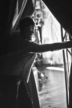 black and white photograph of a woman opening curtains