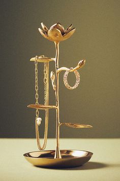 a gold jewelry stand with rings and necklaces hanging from it's sides on a table