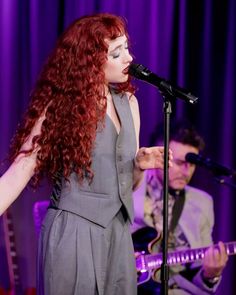 a woman with long red hair standing in front of a microphone and singing into a microphone