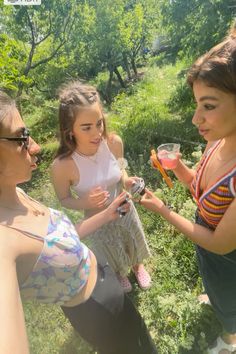 three women are standing in the grass and one is holding a glass with something on it