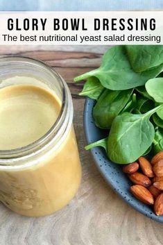 a bowl full of spinach and almonds next to a glass jar filled with dressing