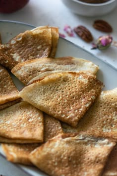 some pancakes on a white plate with fruit in the back ground and nuts scattered around them