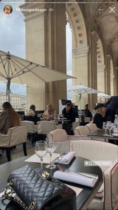 people sitting at tables with umbrellas in an outdoor dining area on a cloudy day