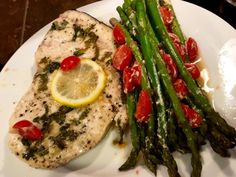 a white plate topped with fish and asparagus next to a lemon wedged slice