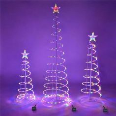 three lighted christmas trees in the shape of spirals with stars on them, against a purple background