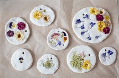 six painted flowers are on white plates with holes in the middle to put them together