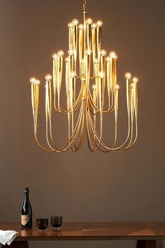 a chandelier hanging over a wooden table with wine glasses and bottle on it