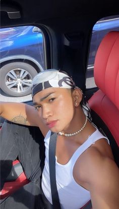 a young man sitting in the back seat of a car wearing a hat and pearl necklace