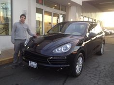 a man standing next to a black porsche cayen