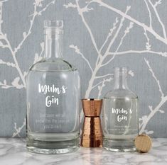 two personalized glass bottles sitting on top of a marble counter next to a copper shaker