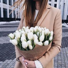 a woman holding a bouquet of white tulips in front of a large building