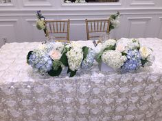 the table is covered with white and blue floral centerpieces, along with gold chairs