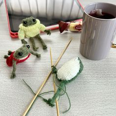 crocheted toys and knitting needles on a table next to a cup of tea