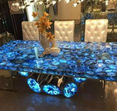 a glass table with blue lights on it in a room filled with white chairs and chandeliers