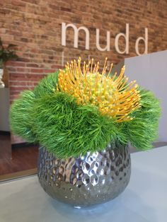 a silver vase filled with green and yellow flowers