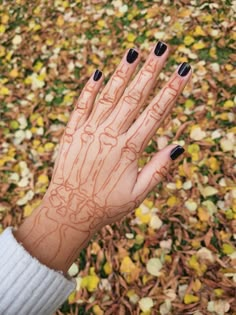 a woman's hand with black and white nail polish on it, surrounded by leaves