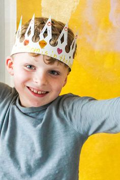 a young boy wearing a crown on top of his head while standing in front of a yellow wall