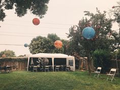 an outdoor party tent with chairs and balloons in the air, set up on grass