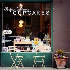 two wooden chairs sitting in front of a window with a sign that says perfect selling cupcakes