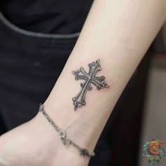 a cross tattoo on the wrist is shown in black and grey colors, with a chain around it