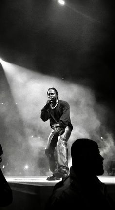 a man standing on top of a stage with his hands in his pockets while talking on a cell phone