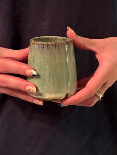 a woman's hands holding a green cup with nail polishes on her nails