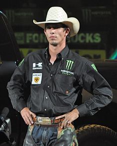 a man wearing a cowboy hat standing next to a truck with his hands in his pockets