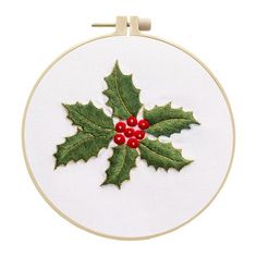 an embroidered holly leaf with red berries is shown in this embroidery pattern on a white hoop