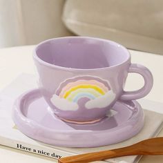 a purple cup and saucer sitting on top of a white table next to a wooden spoon