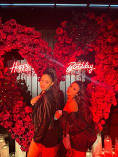 two women standing next to each other in front of a heart shaped display with candles