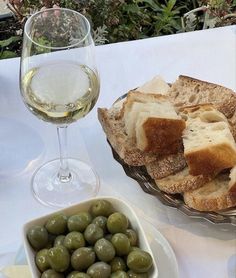 bread and olives are on a table next to a glass of white wine,